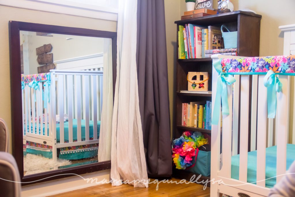 A low mirror and a bookshelf with some toys and dress up clothes for a toddler play space in a bedroom