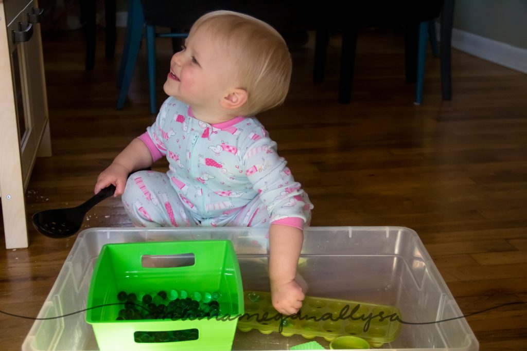 a toddler smiling while playing with the green water bead sensory bin