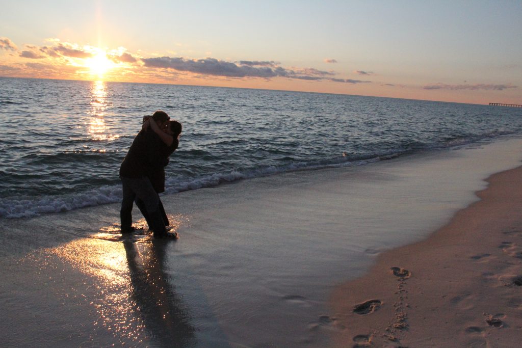 a young couple kissing on the beach at sunset with the waves at their feet