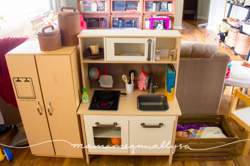 a dramatic play home space with an ikea play kitchen, play fridge and wooden crate for a baby crib