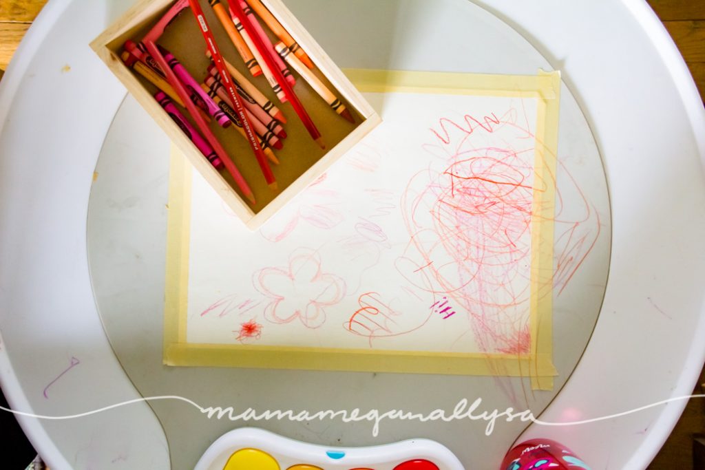 a white play table with a peice of paper taped down with toddler scribbles all over it