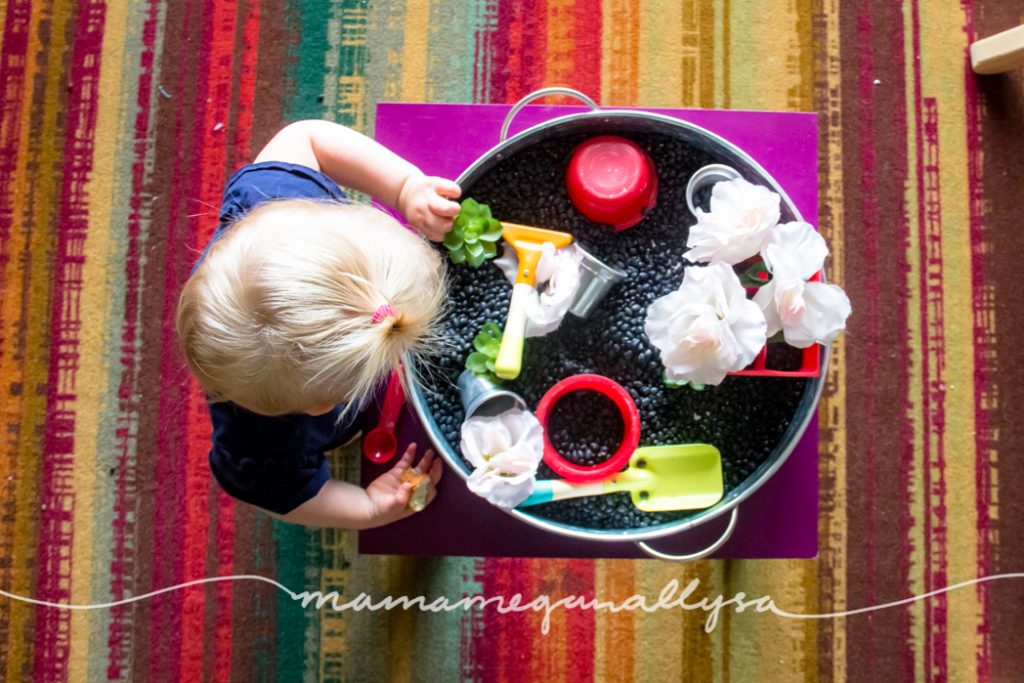 Top down view of a toddler playing in a black bean garden sensory bin