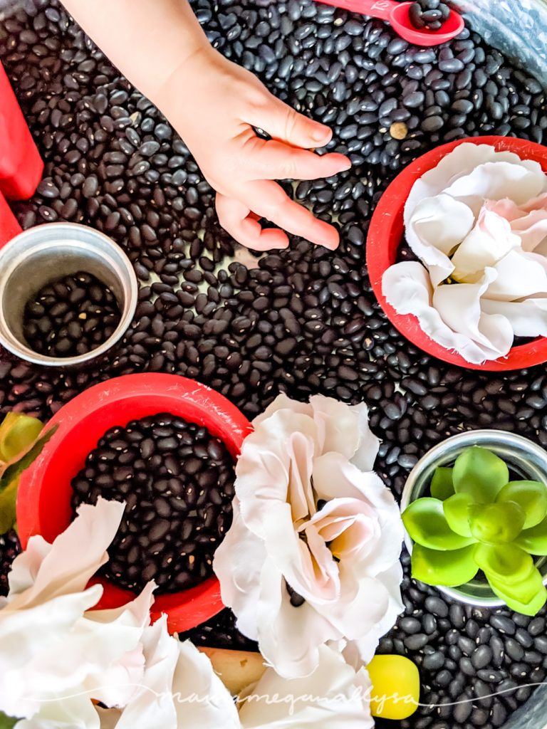 close up of a toddler pinching a black bean inside of a garden sensory bin