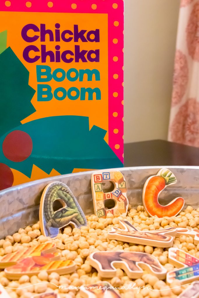 a close up of the puzzle letters in the tray of chick peas with Chicka Chikca Boom Boom book propped up behind the tray