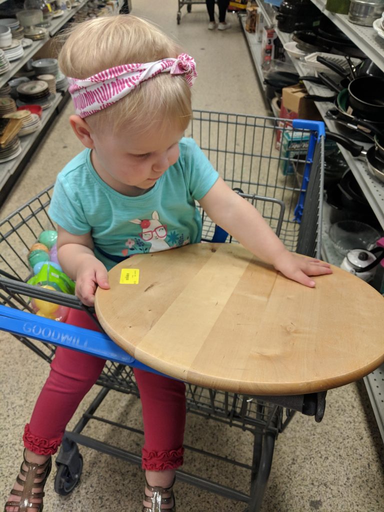 a toddler holding a wooden lazy susan in Goodwill after months of searching