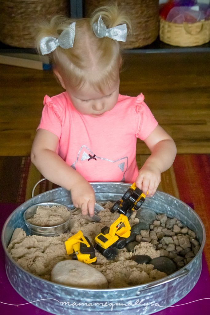 a toddler loading up a construction truck with sand