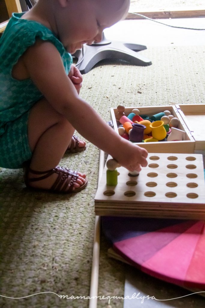 a toddler happily inserting wooden peg people into the peg board