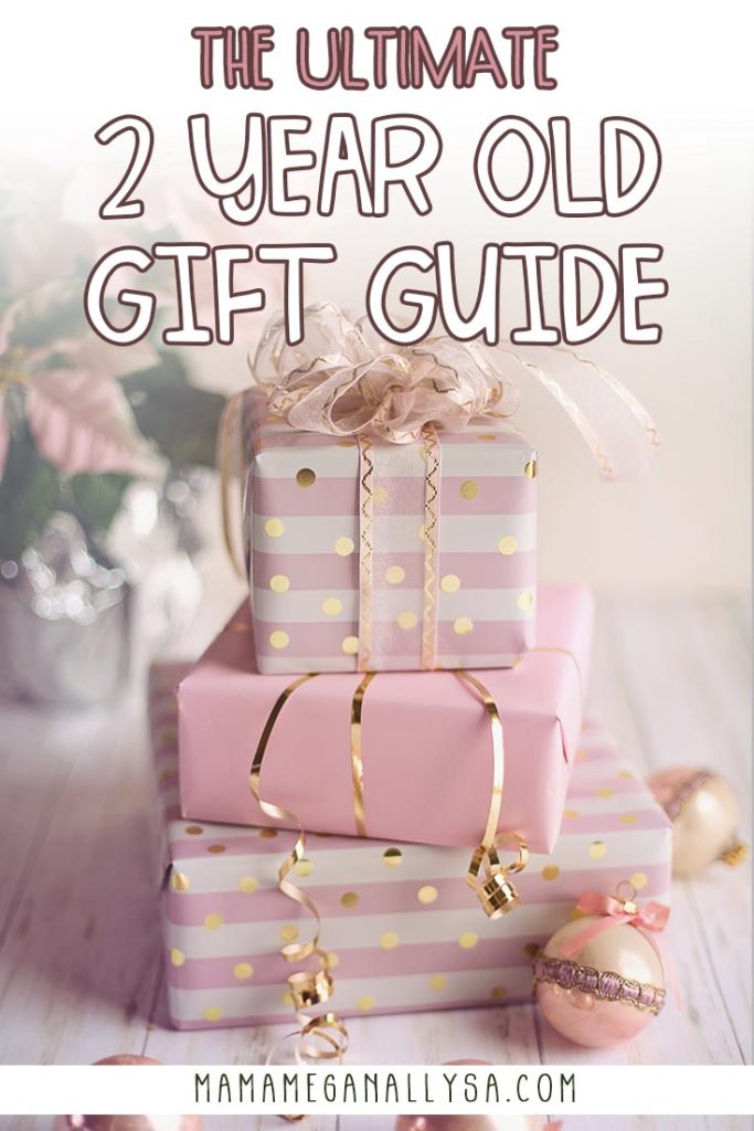 a pin image that reads the ultimate 2 year old gift guide with a stack of pink and gold wrapped presents with ornaments scattered around