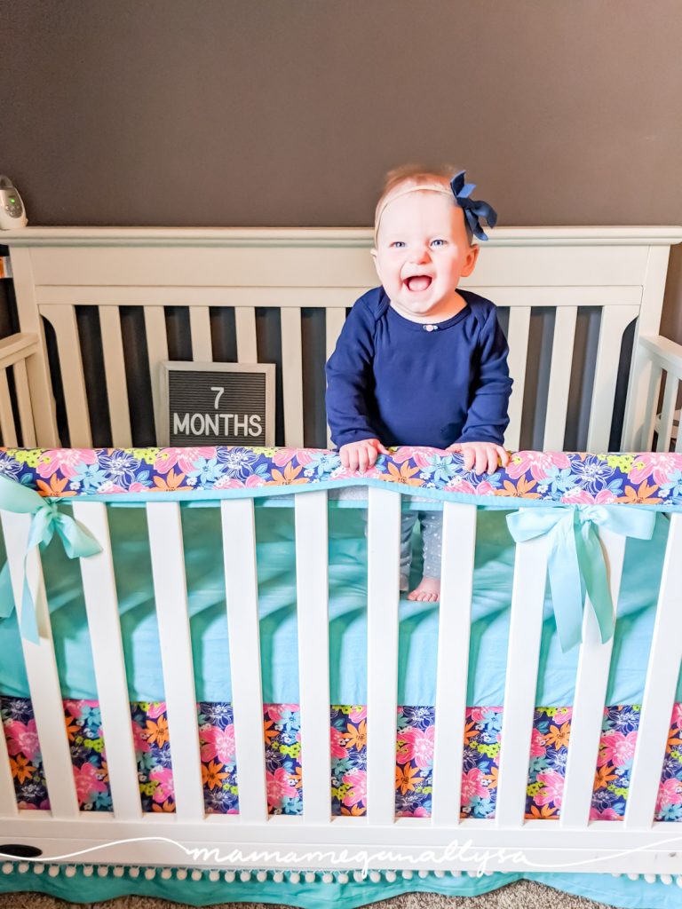 a baby girl standing in a crib with a letterboard that says 7 months