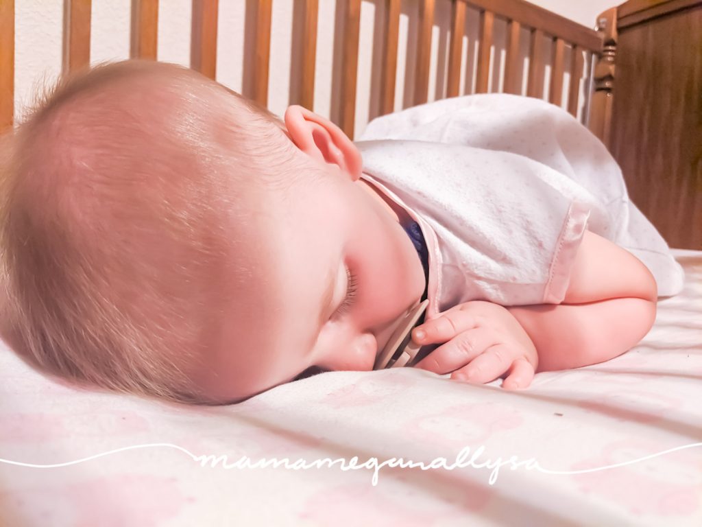 a close up of a baby with a pacifier asleep in a crib