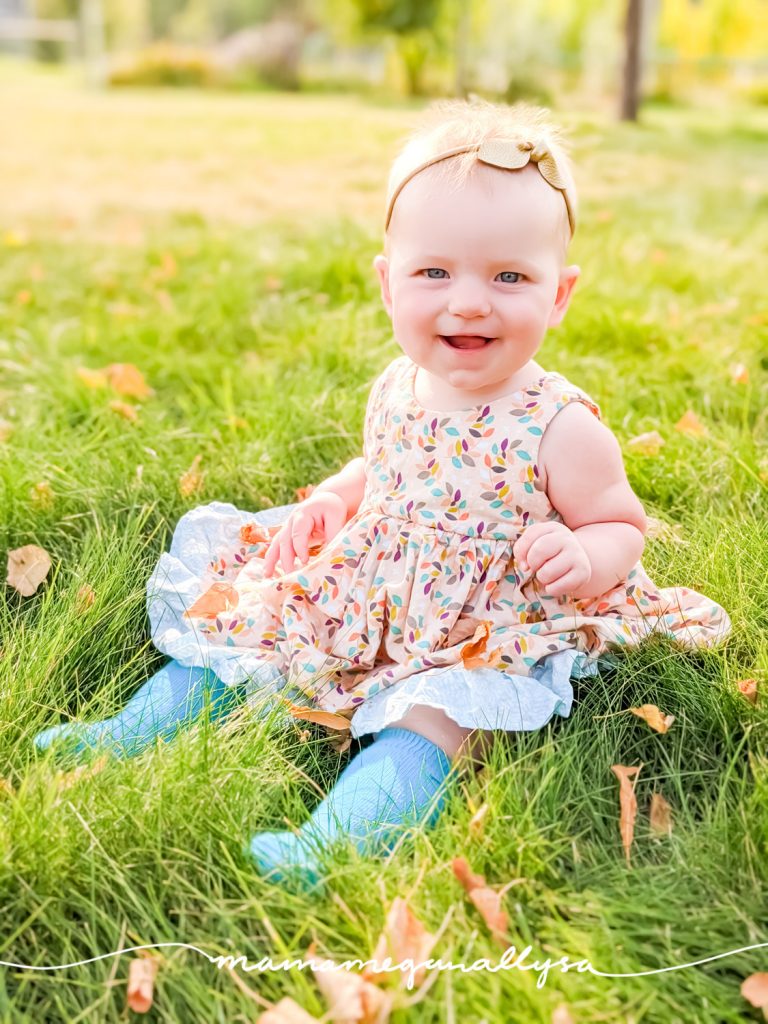 baby girl in a dress sitting in the grass surrounded my fall leaves