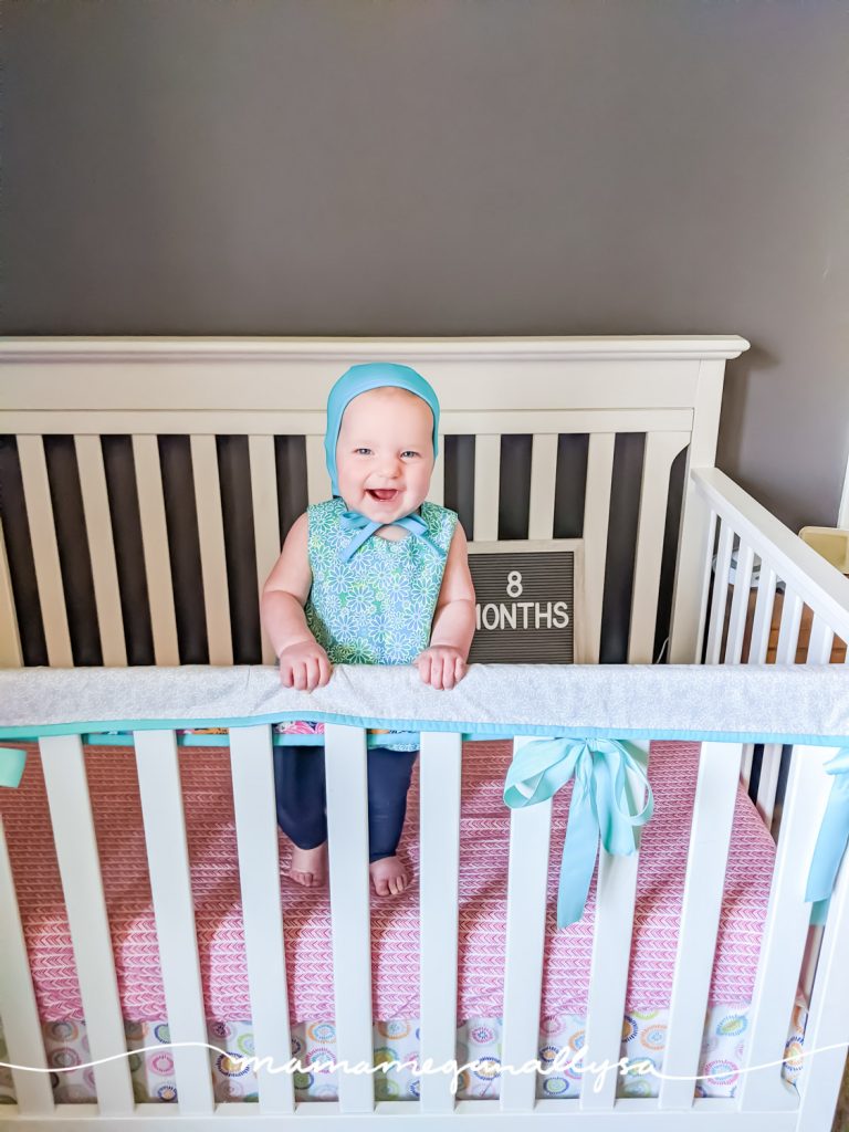 a baby girl standing in a crib with a letterboard that says 8 months