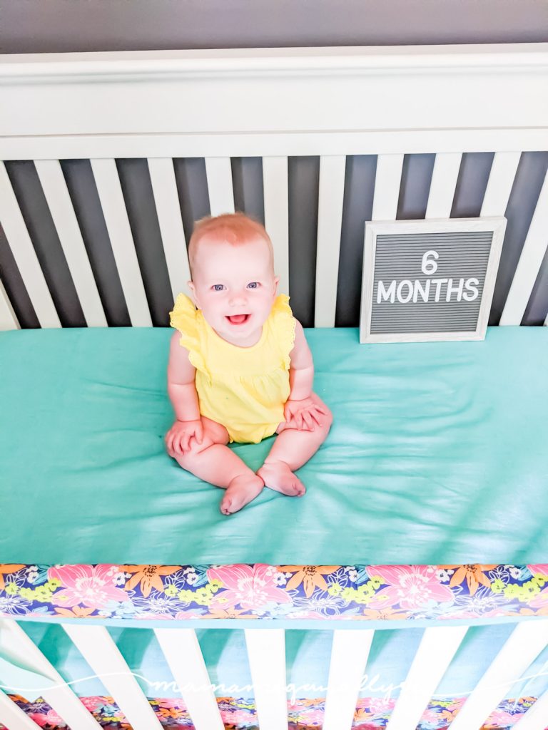 a baby girl sitting in a crib with a letterboard that says 6 months