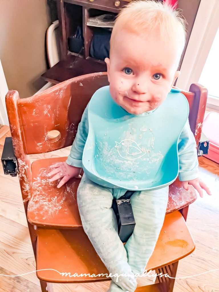 a baby and wooden highchair, both completely smeared in yogurt