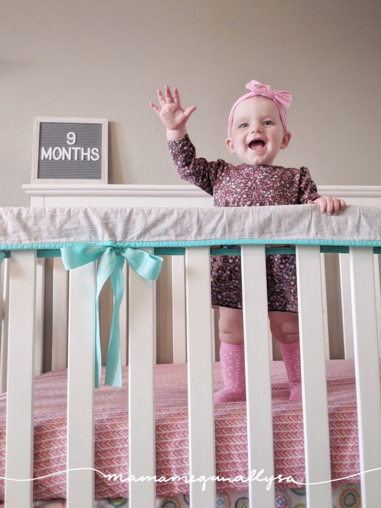 a baby girl standing in a crib with a letterboard that says 9 months