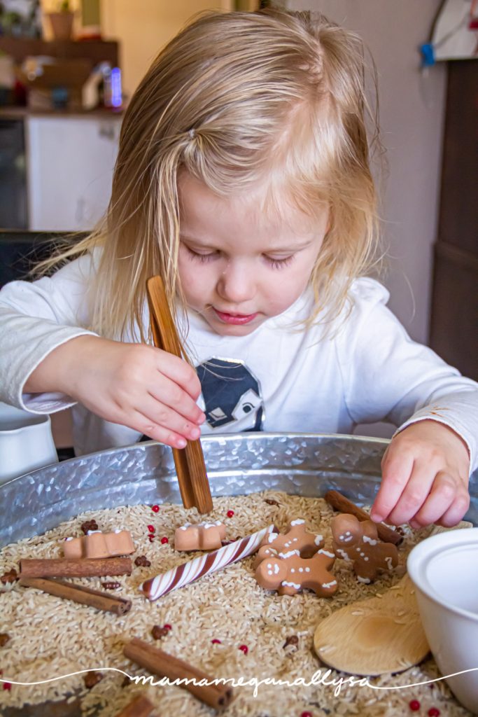 a toddler practicing with some wooden tongs in the gingerbread sensory bin