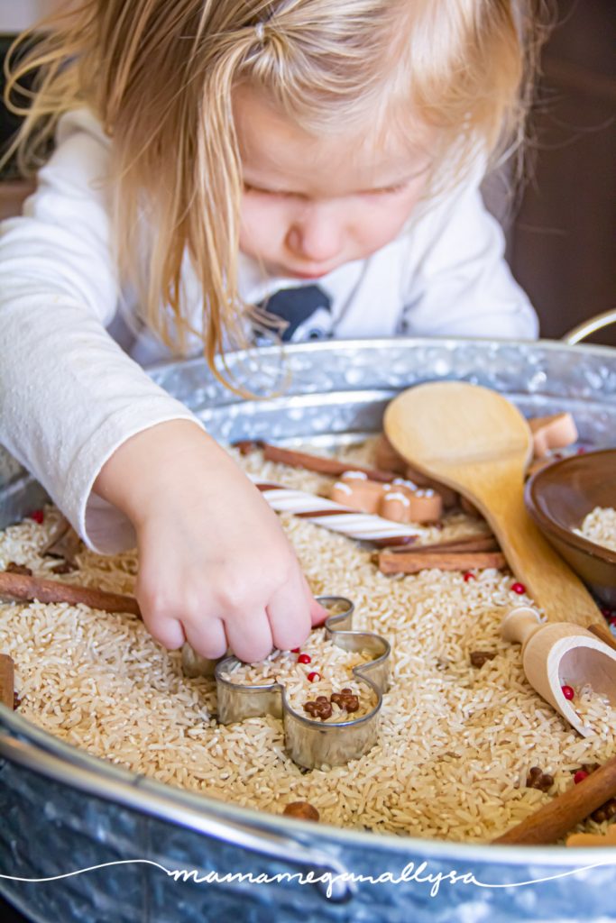 a toddler playing in a gingerbread sensory bin placing sprinkles as the buttons on a gingerbread man