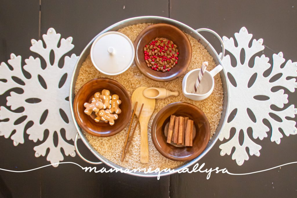 an overhead shot of the gingerbread sensory bin with three bowls of extras to add to the gingerbread rice. as well as three tools, and a sugar and creamer set for pouring