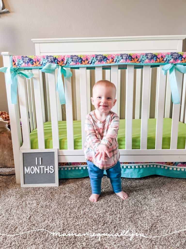 a baby girl standing in front of her crib with a letter board that says 11 months