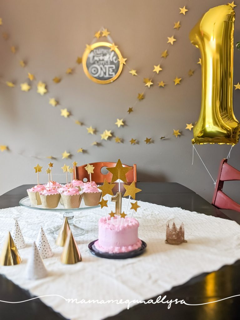 twinkle twinkle little one theme for a simple 1st birthday celebration at home with a pink smash cake and gold stars on top. gold star stands along the wall and a gold 1 balloon 