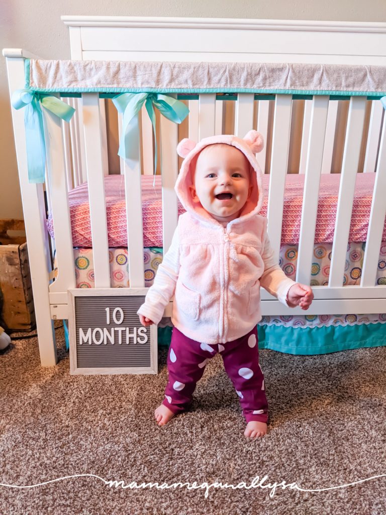 a baby girl standing in front of her crib with a letter board that says 10 months