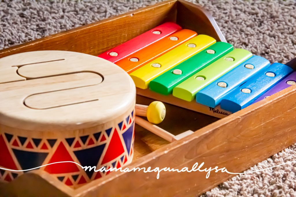 a close-up shot of a wooden toy drum and a wooden xylophone sitting in a wooden tray