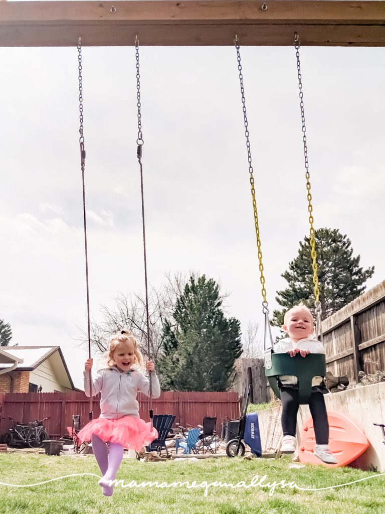 two little girls smiling and swinging in their backyard