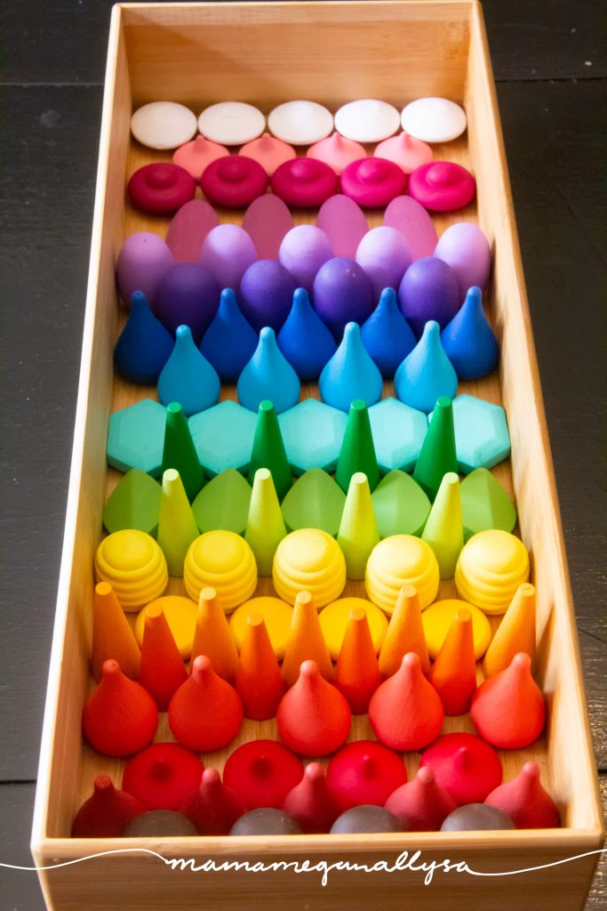 a wooden tray filled with a pattern of wooden loose parts in rainbow order