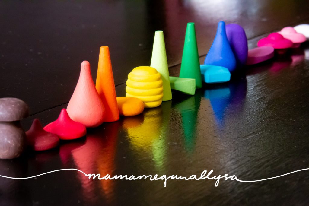 a long line of wooden loose parts all painted and arranged in ROYGBIV order on a black table