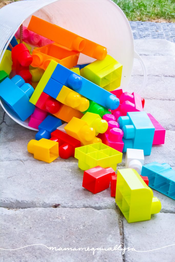 some Megablocks spilling out of a bucket on the patio in the back yard