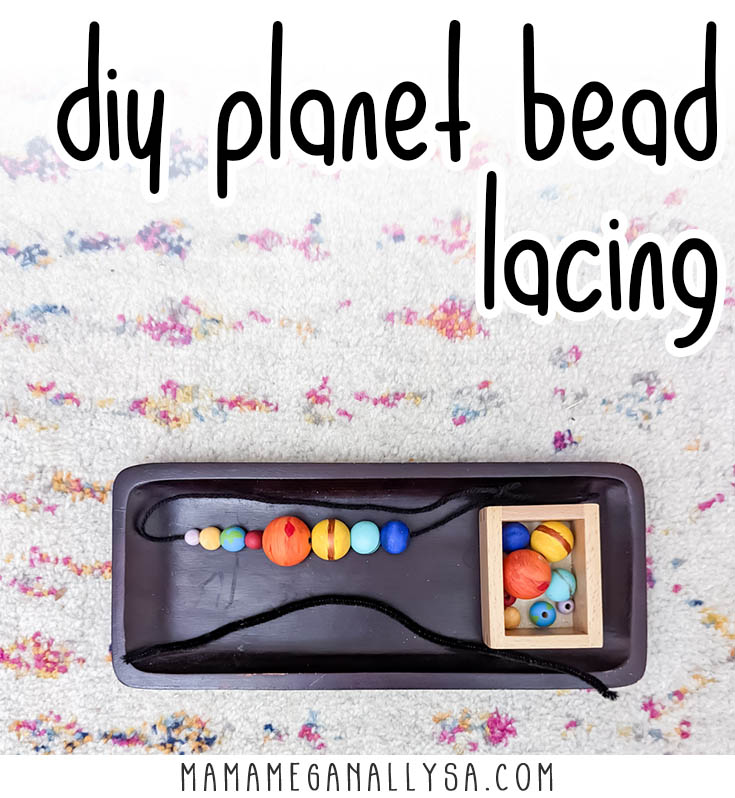 a string of wooden beads painted to represent the planets lays on a dark tray with a little box holding another set of beads to be strung on the pipe cleaner on the tray