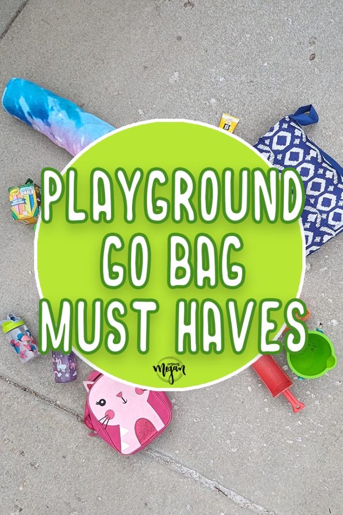 a pin image that reads playground go bag must haves  centered over a green circle. Hidden behind the circle you can see bits of a number of items laid out on the concrete. A blue picnic blanket, a small pink kitty backpack, a couple of water bottles, a box of chalk and a tie-dye towel are all partially visible.