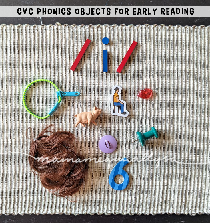 an image of a woven mat with a wooden letter /i/ at the top. Below it are a collection of CVC phonics objects. A zip(per) pig, sit magnet, lip, wig, lid, pin, and six
